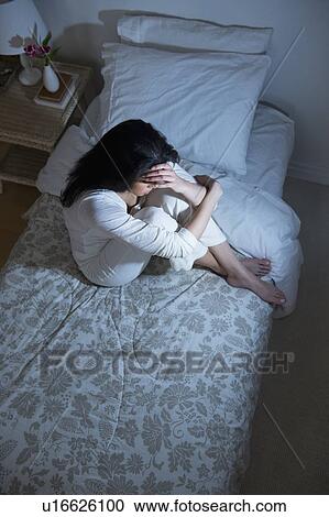 Stock Image - Young woman sitting on bed. Fotosearch