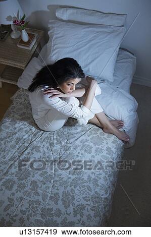 Stock Photo - Young woman sitting on bed. Fotosearch