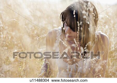 Picture - Young woman sitting on cornfield. Fotosearch