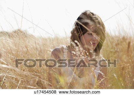 Stock Photo - Young woman sitting on cornfield. Fotosearch