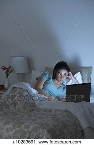 Stock Image - Young woman using laptop in bed. Fotosearch