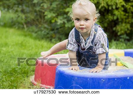 Stock Image - Baby girl climbing in sandbox. Fotosearch