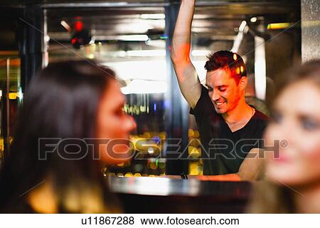 Stock Photo - Bartender waving to customers in bar. Fotosearch