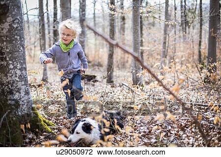 Stock Image - Boy and dog exploring in forest. Fotosearch