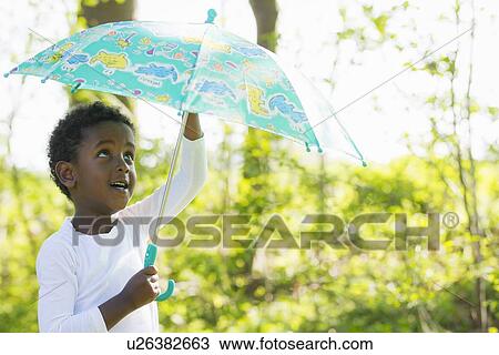 Stock Image - Boy carrying umbrella in forest. Fotosearch