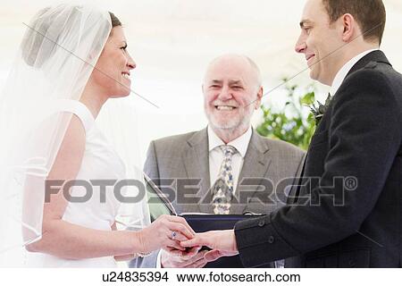 Picture - Bride putting ring on grooms finger. Fotosearch