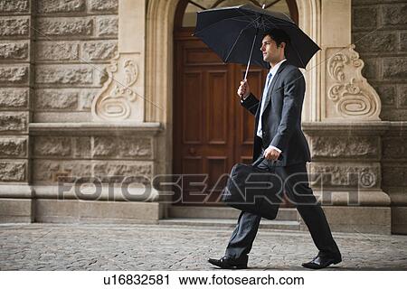 Stock Image - Businessman carrying umbrella on street. Fotosearch