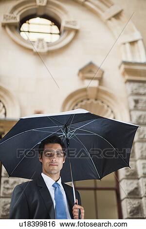 Stock Photograph - Businessman carrying umbrella on street. Fotosearch