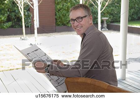 Businessman reading blueprints in chair View Large Photo Image Stock Photography - Businessman reading blueprints in chair. Fotosearch