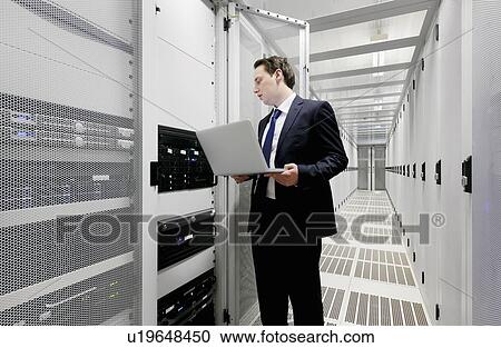 Stock Image - Businessman using laptop in server room. Fotosearch