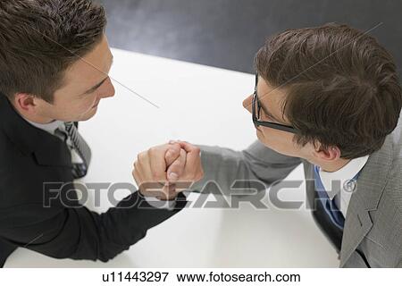 Stock Photo - Businessmen arm wrestling in office. Fotosearch