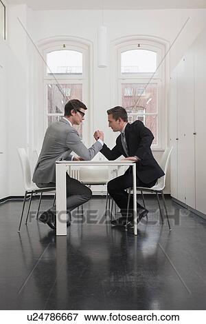Businessmen arm wrestling in office View Large Photo Image Stock Photo - Businessmen arm wrestling in office. Fotosearch