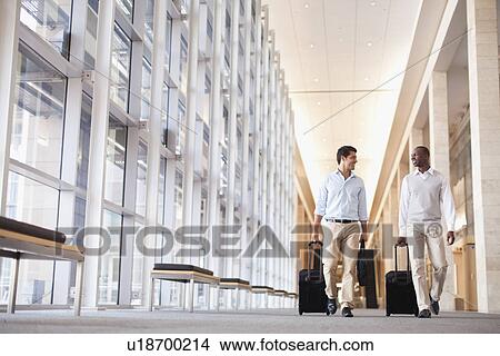 Picture - Businessmen rolling luggage in hallway. Fotosearch