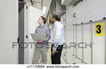 Picture - Businessmen using laptop in server room. Fotosearch