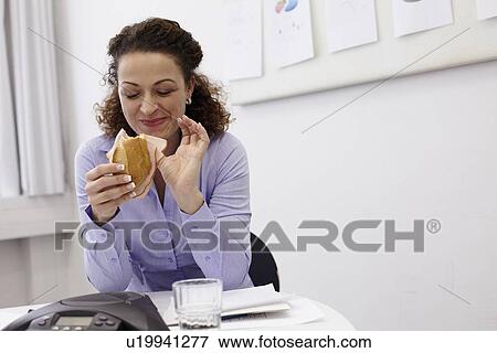 Businesswoman eating at desk in office View Large Photo Image Stock Photo - Businesswoman eating at desk in office. Fotosearch