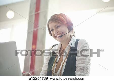 Stock Photo - Businesswoman wearing headset at desk. Fotosearch