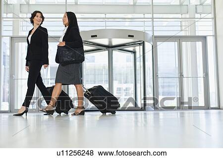Businesswomen rolling luggage in lobby View Large Photo Image Stock Photo - Businesswomen rolling luggage in lobby. Fotosearch
