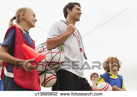 Stock Image - Coach carrying soccer balls on pitch. Fotosearch