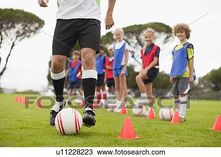 Stock Image - Coach training childrens soccer team. Fotosearch