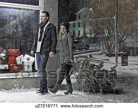 Couple carrying Christmas tree in snow View Large Photo Image Stock Image - Couple carrying Christmas tree in snow. Fotosearch