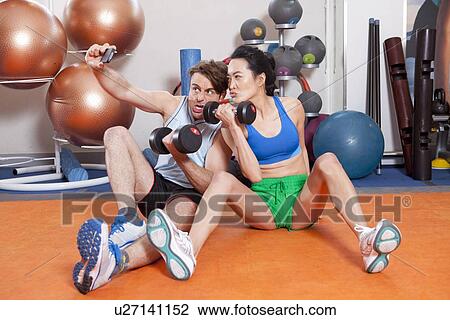 Stock Image - Couple lifting weights in gym. Fotosearch