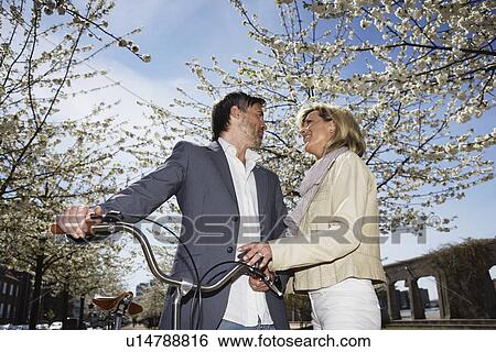 Stock Photograph - Couple standing with bicycle in park. Fotosearch