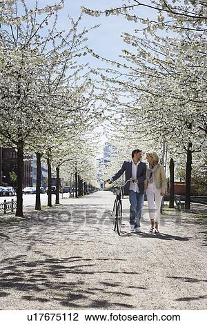 Couple walking bicycle in park View Large Photo Image Stock Image - Couple walking bicycle in park. Fotosearch