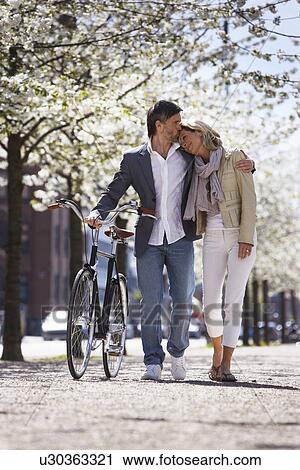 Stock Image - Couple walking bicycle in park. Fotosearch