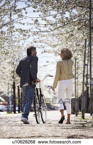 Couple walking bicycle in park View Large Photo Image Stock Photo - Couple walking bicycle in park. Fotosearch