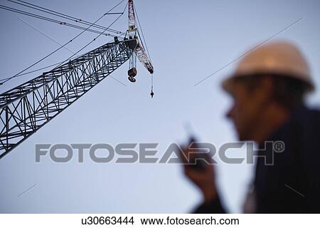 Picture - Crane over worker at oil refinery. Fotosearch