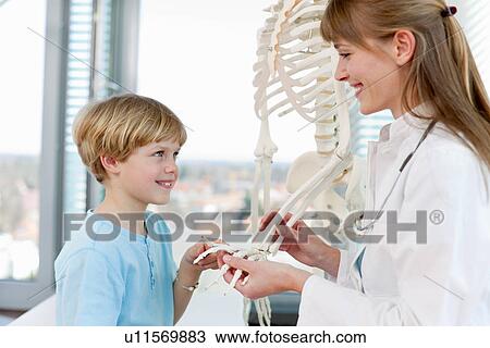 Stock Image - Doctor showing skeletal model to patient. Fotosearch