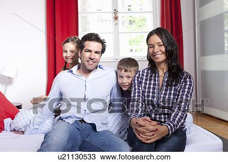 Stock Image - Family smiling together on bed. Fotosearch