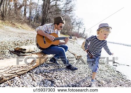 Stock Image - Father and son with guitars by creek. Fotosearch