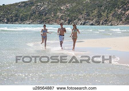Stock Photo - Friends running in waves on beach. Fotosearch