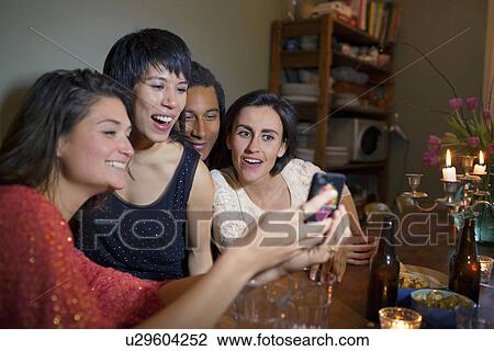 Stock Image - Friends using cell phone at dinner table. Fotosearch