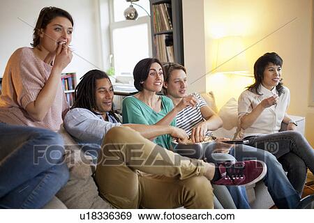 Stock Photo - Friends watching a movie in living room. Fotosearch