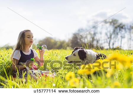 Girl blowing bubbles with dog in field View Large Photo Image Picture - Girl blowing bubbles with dog in field. Fotosearch