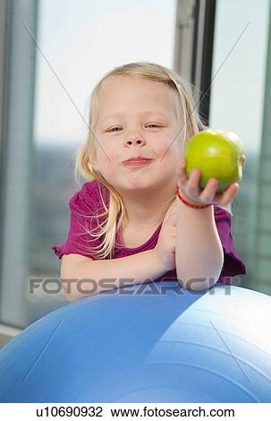 Stock Image - Girl eating apple on exercise ball. Fotosearch