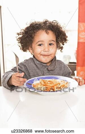 Stock Photo - Girl eating pasta with sauce at table. Fotosearch