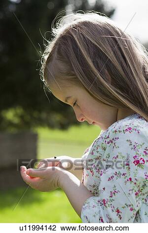 Stock Image - Girl examining insect on hand outdoors. Fotosearch