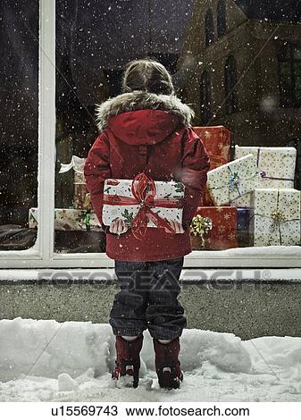 Stock Image - Girl holding Christmas present in snow. Fotosearch
