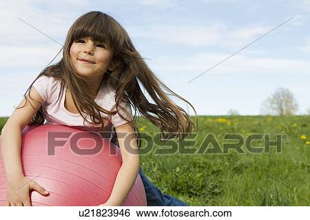 Stock Photograph - Girl playing on bouncy ball in field. Fotosearch