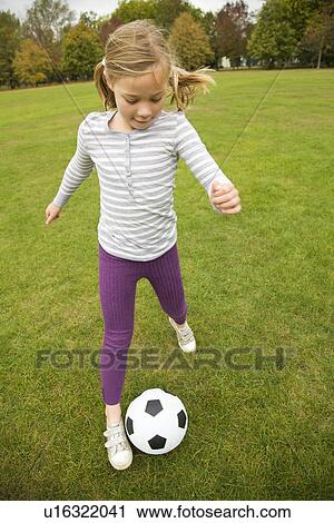 Stock Image - Girl playing with soccer ball in field. Fotosearch