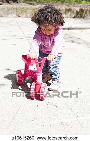 Stock Image - Girl playing with tricycle in park. Fotosearch