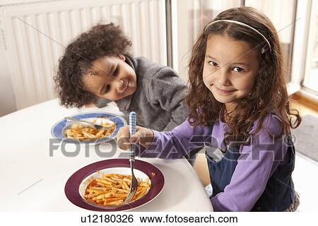 Girls eating pasta together at table View Large Photo Image Stock Photograph - Girls eating pasta together at table. Fotosearch