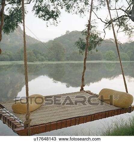 Stock Image - Hammock on tree by still rural lake. Fotosearch