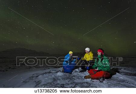 Stock Photography - Hikers relaxing under aurora borealis. Fotosearch