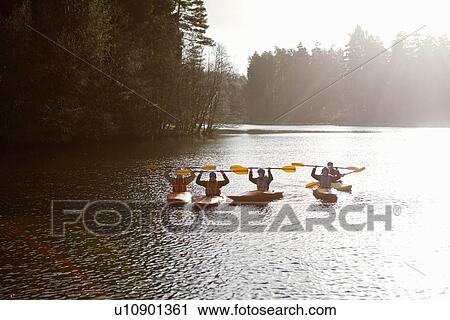 Stock Image - Kayakers holding oars on still lake. Fotosearch