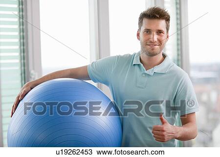 Stock Image - Man carrying exercise ball in gym. Fotosearch
