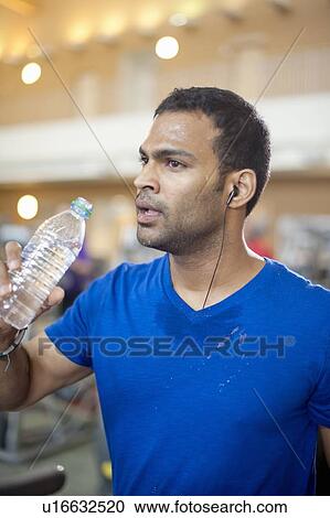 Stock Image - Man drinking water bottle in gym. Fotosearch